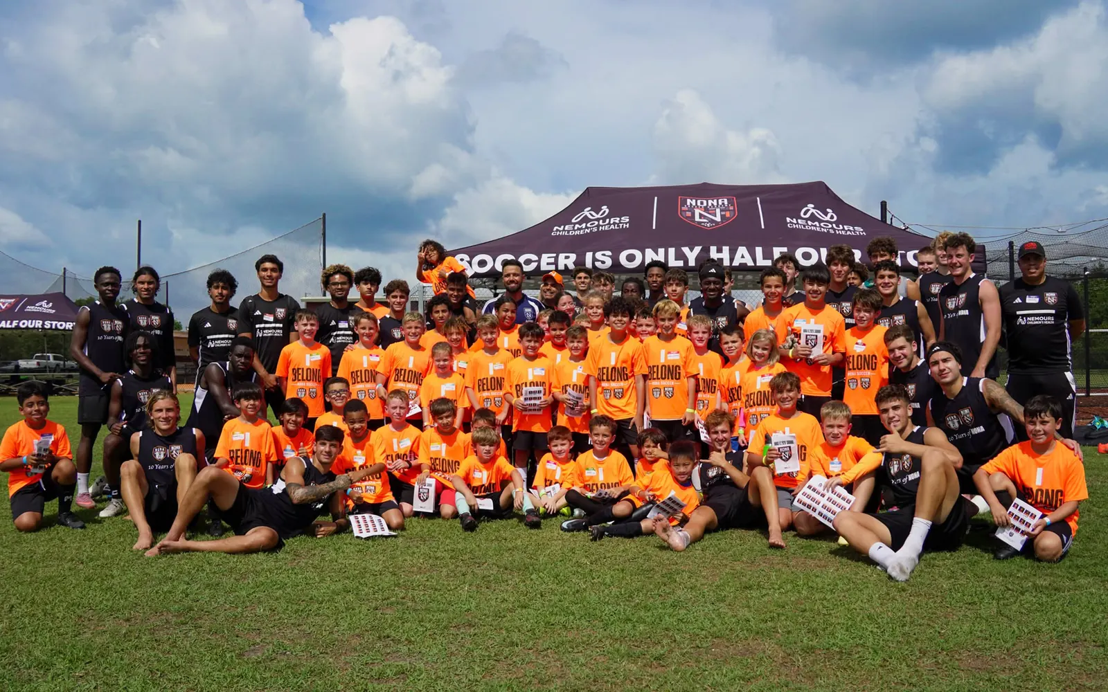 Grupo grande de atletas da Nona Soccer Academy, de uniforme laranja, posando juntos no campo