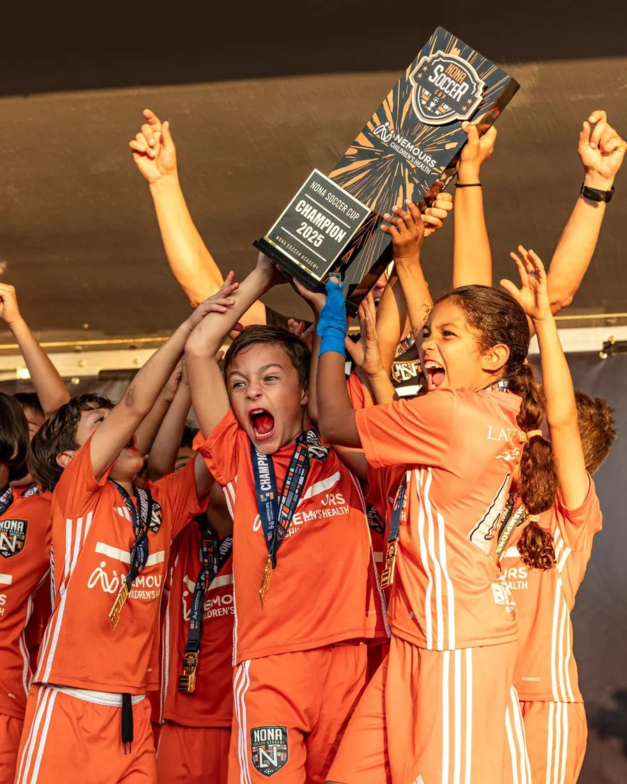 Atletas da Nona de uniforme laranja erguem o troféu da Nona Cup