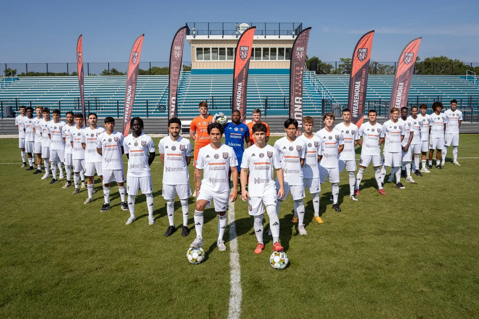 Elenco do Nona FC, de uniforme branco, perfilado em campo diante das bandeiras #WeAreNona
