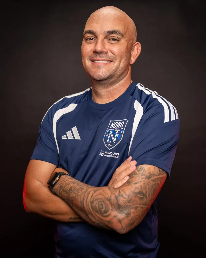 Fábio Silva, fundador e CEO da Nona Soccer Academy, de braços cruzados, com camisa azul-marinho do clube
